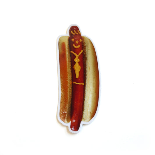 A die cut sticker of a hotdog with a smiley face and tie drawn on with mustard