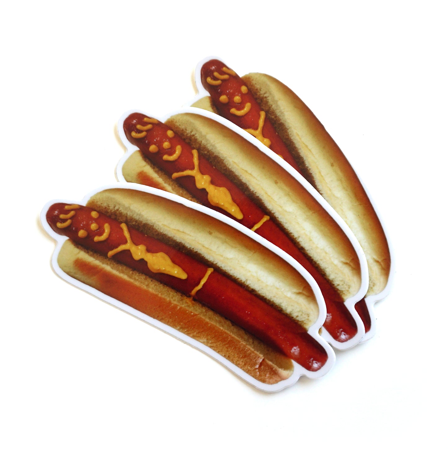 Photo of 3 die cut stickers of a hotdog with a smiley face and tie drawn on with mustard on a white background