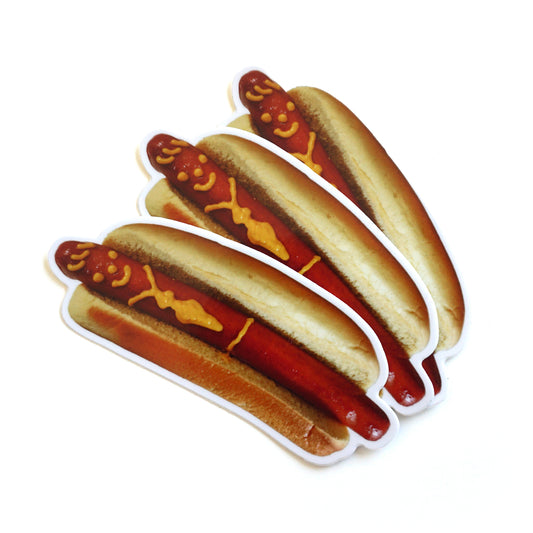 Photo of 3 die cut stickers of a hotdog with a smiley face and tie drawn on with mustard on a white background
