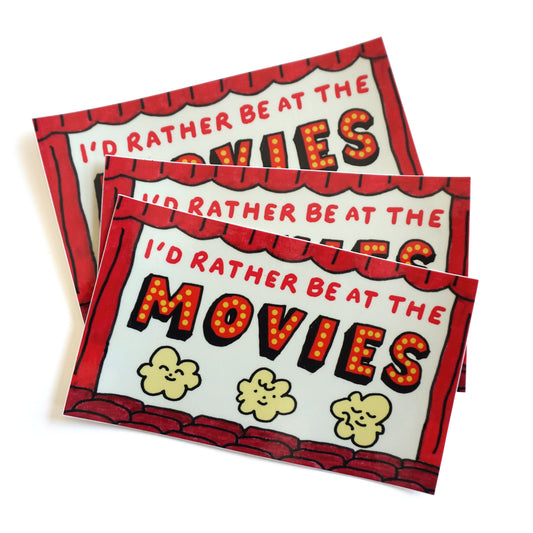 Stack of 3 stickers that say "Id' rather be at the movies" with 3 illustrated popcorn characters underneath the text with theater curtains and seats along the borders